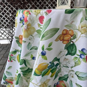Könnte beinhalten: Weiße Tischdecke mit einem floralen Muster mit gelben Blumen, grünen Blättern, roten Beeren und orangenen Früchten. Die Tischdecke hat einen weißen Hintergrund und ist aus einem weichen, leinenartigen Stoff gefertigt.