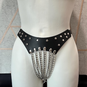 May include: Black leather harness with silver metal studs and chains. The harness is designed to be worn around the waist and has a chain that hangs down the front.