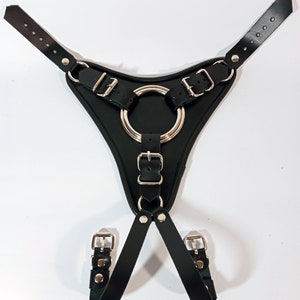 May include: Black leather harness with silver metal buckles and a large silver ring. The harness has two straps that connect to the ring.