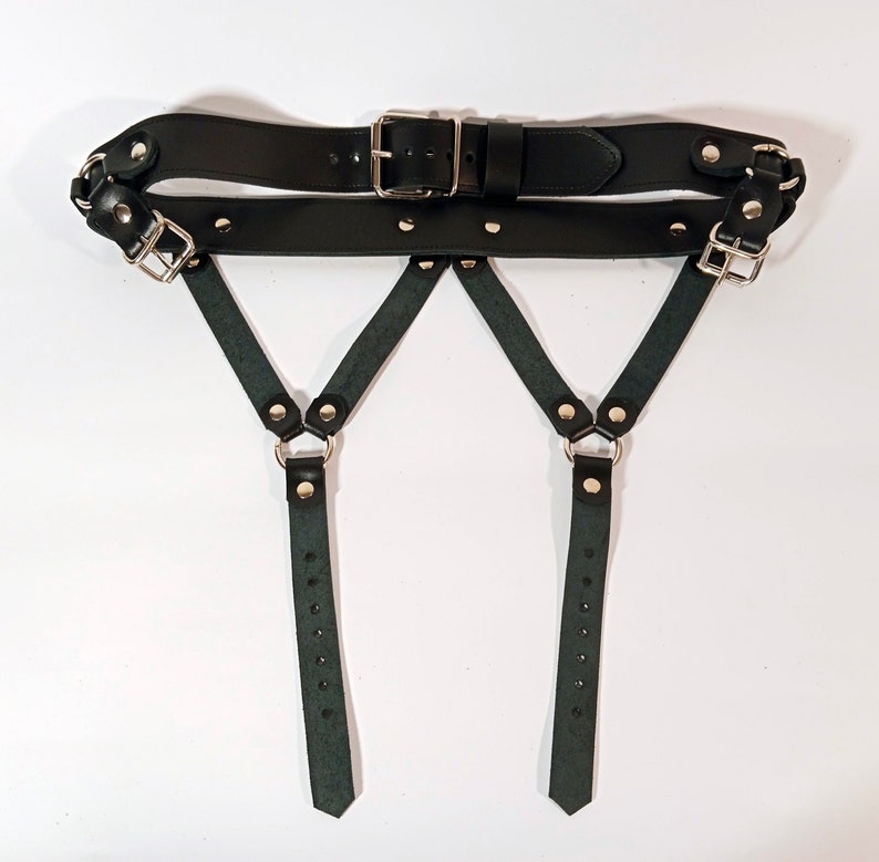 May include: Black leather harness with two straps and silver buckles. The straps are adjustable and have silver rings at the bottom.