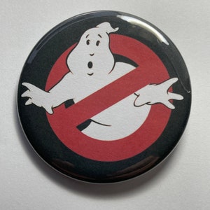 May include: A black and red button with a white ghost in a no symbol. The ghost has a surprised expression and is wearing a red slash across its body.