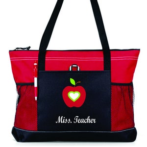 May include: Red and black tote bag with a zipper closure and a mesh pocket. The bag has an embroidered apple with a heart in the center and the text "Miss. Teacher".