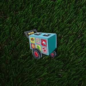May include: A blue and white ice cream cart pin with colorful ice cream illustrations. The cart has a handle and wheels.