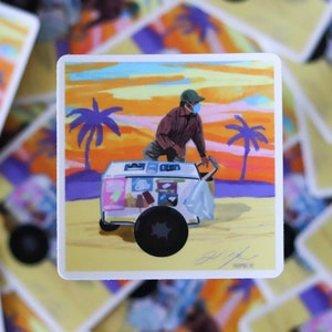 May include: A person wearing a face mask and a baseball cap pushes a white ice cream cart with a blue and white awning. The cart is on a beach with palm trees and a sunset in the background.