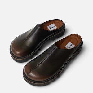 May include: A pair of dark brown leather slip-on mules with a rounded toe, a thick black lug sole, and a visible center seam. The interior footbed features a white label with the black text te. shoes KYIV printed on the heel area of each shoe.
