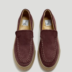 May include: A pair of dark burgundy suede slip-on shoes featuring a moccasin-style stitched toe seam with a scalloped edge detail. The shoes have a thick, light-coloured ridged rubber sole and a white interior label reading te. shoes KYIV.