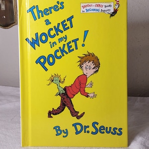 May include: A yellow book cover with the title "There's a WOCKET in my POCKET!" in blue text. The book is by Dr. Seuss and is part of the "Bright and Early Books for Beginning Beginners" series. The cover features an illustration of a boy with a green creature sticking out of his back pocket.