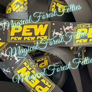 May include: Black and yellow ribbon with the text "PEW PEW PEW" and a star wars spaceship graphic. The ribbon is folded and stacked on top of itself.