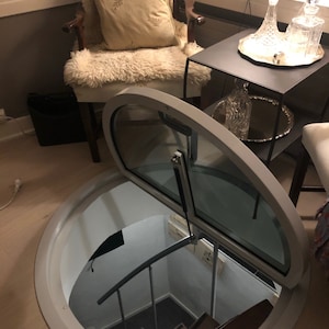 May include: A white circular trapdoor with a glass door that opens to reveal a spiral staircase leading down into a basement.