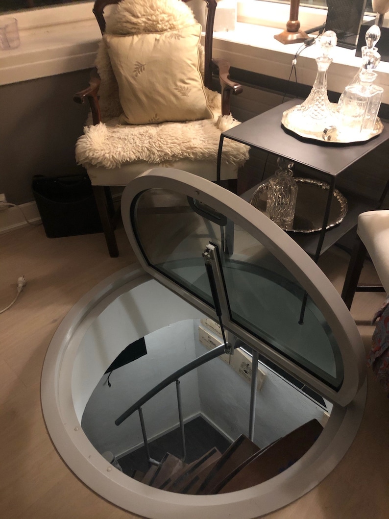 May include: A white circular trapdoor with a glass door that opens to reveal a spiral staircase leading down into a basement.