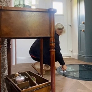 May include: A wooden table with a drawer and turned legs, a wooden box with handles, and a round glass panel in the floor.