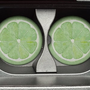 May include: Two lime green coasters with a white lime design in the shape of a lime wedge. The coasters are in a cassette tape case.