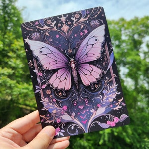 May include: A purple and pink butterfly with white spots on its wings is surrounded by intricate floral designs on a black background. The butterfly is the focal point of the image, with the floral designs creating a frame around it.