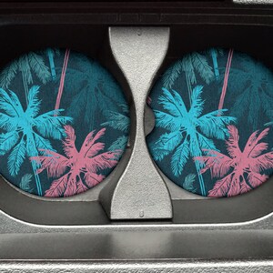 May include: Two round drink coasters with a tropical palm tree design. The coasters feature a dark blue background with pink and blue palm trees.