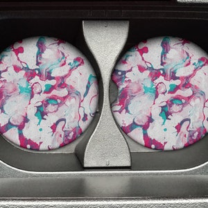 May include: Two round drink coasters with a white background and a pink, blue, and black marbled design.