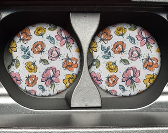 May include: Two round coasters with a floral pattern. The coasters feature a white background with pink, orange, and yellow flowers and green leaves.