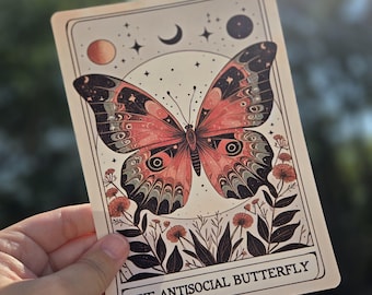 Könnte beinhalten: Rechteckige Karte mit einer detaillierten Illustration eines Schmetterlings mit roten, schwarzen und grauen Flügeln. Die Karte hat ein Himmelsdesign mit Sternen, einem Halbmond und dem Text "THE ANTISOCIAL BUTTERFLY".
