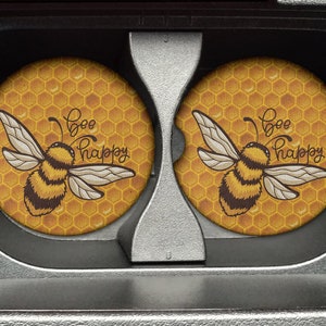 May include: Two yellow and black bee coasters with a honeycomb pattern and the text "Bee Happy".