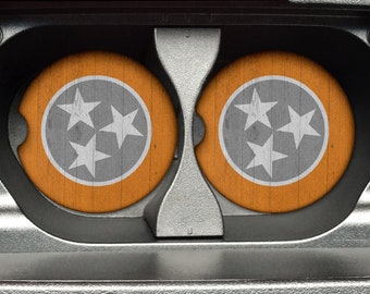 May include: Two round coasters with a wood grain texture. Each coaster features a white circle with three white stars in the centre, representing the state flag of Tennessee.