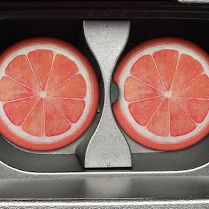 May include: Two round, orange and white grapefruit coasters with a segmented design. The coasters are placed in a cassette tape holder.