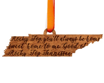 May include: Wooden ornament shaped like the state of Tennessee with the text "Rocky Top, you'll always be home sweet home to me. Good ol' Rocky Top Tennessee" engraved on it. The ornament is hanging from a bright orange ribbon.