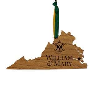 May include: A wooden ornament shaped like the state of Virginia, featuring a dark brown engraved monogram, the text "WILLIAM & MARY", and a small star. A green and yellow ribbon is attached to the top for hanging, showcasing a natural wood grain.