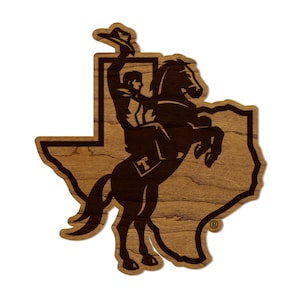 May include: A brown wooden cutout of the state of Texas with a silhouette of a cowboy riding a horse. The cowboy is wearing a hat and is holding onto the reins. The horse is rearing up on its hind legs. The cutout is on a white background.