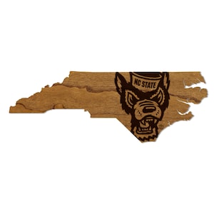 May include: A wooden outline of the state of North Carolina with a brown wolf mascot logo in the center. The logo includes the text "NC STATE".