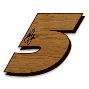 May include: Wooden number five with a dark brown border and a light brown wood grain finish. The number has a signature in the upper left corner. The number is a decorative item.