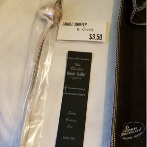 May include: A silver candle snuffer in a clear plastic bag with a white price tag that reads "CANDLE SNUFFER by Gerity $3.50". The snuffer is packaged with a black velvet pouch that reads "Pacific Silvercloth Prevents Tarnish".