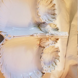 Puede incluir: Plato de servir de porcelana blanca con tres secciones, cada una con forma de concha. El plato tiene un borde dorado alrededor de los bordes y un diseño dorado en las conchas.