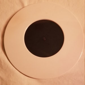 Puede incluir: Alfombrilla circular blanca para tocadiscos con un agujero central negro.