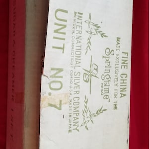 May include: A vintage cardboard box for a sugar and creamer set. The box is labelled "Unit No. 7" and features the text "International Silver Company" and "Springtime Fine China". The box is off-white with green text and accents.