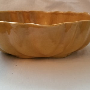 May include: A large, yellow ceramic bowl with a scalloped rim. The bowl is glazed and has a smooth, shiny finish.