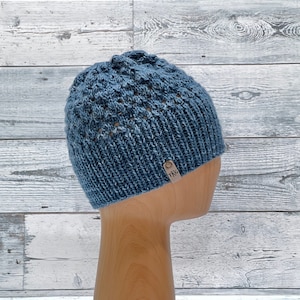 May include: A blue knitted beanie with a textured pattern and a small brown leather tag that says "TKG".