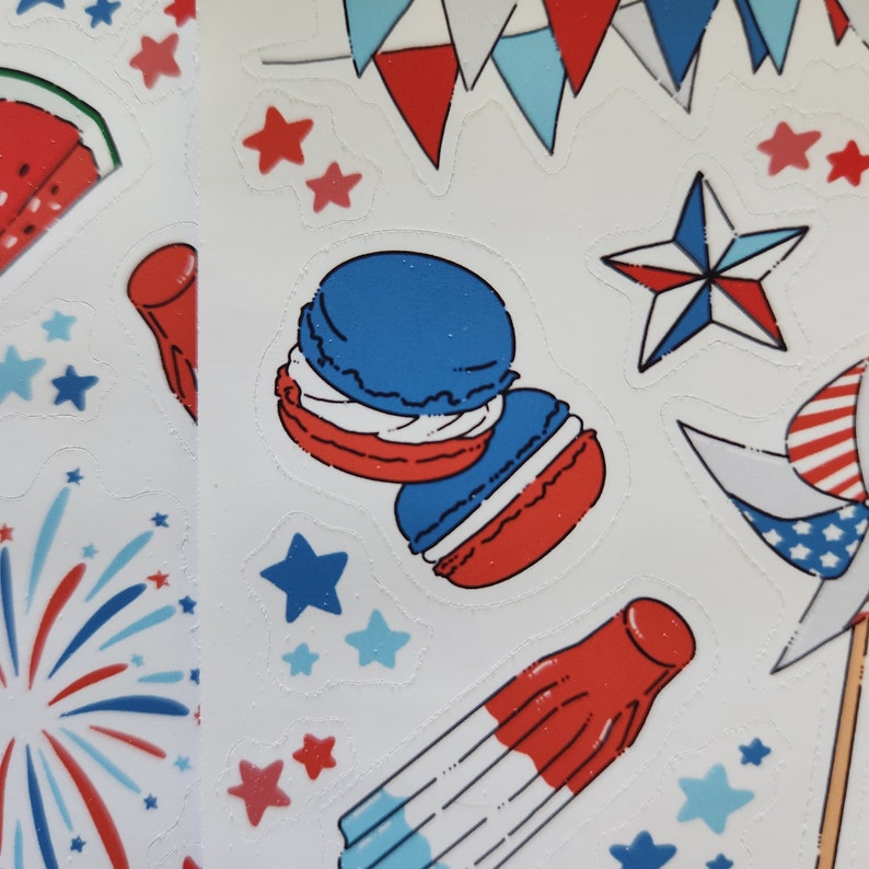 May include: A sheet of stickers featuring various red, white and blue designs, including stars, fireworks, macarons and a popsicle. The stickers are ideal for adding a festive touch to crafts, gifts or home decor.