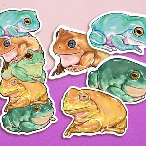 Puede incluir: Un conjunto de nueve pegatinas de ranas con diferentes poses y colores. Las pegatinas están sobre un fondo rosa y morado.