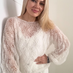 May include: A white, open-weave sweater with a delicate lace pattern. The long-sleeved top has a round neckline and a loose fit. The sweater is made of a soft, lightweight material, perfect for layering.