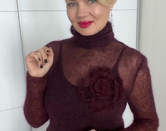 Un delicado y ligero suéter de mohair de cabra, con cuello alto y decoración floral.