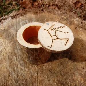 May include: A small wooden box with a lid. The lid is carved with the constellation Hercules and the word "Hercules". The box is made of natural wood and has a rustic look.