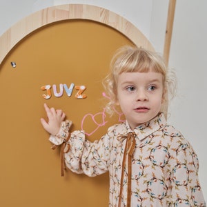 Child playing with magnets on a mustard yellow arch magnetic board for kids