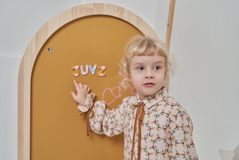 Child playing with magnets on a mustard yellow arch magnetic board for kids
