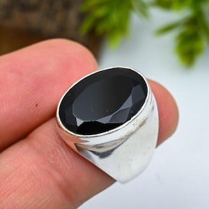 Peut inclure: Une bague en argent ornée d'une grosse pierre noire de forme ovale. La pierre précieuse facettée capte la lumière et présente une surface brillante. La bague a un anneau simple et poli.
