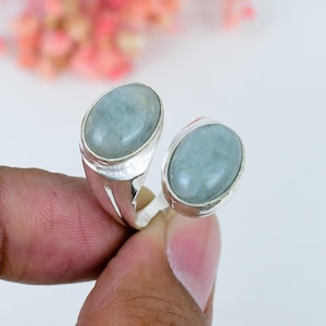 Op de afbeelding: Een open ring van gepolijst zilver, voorzien van twee ovale, gladde, lichtgroene cabochon-edelstenen in eenvoudige metalen zettingen. Het open ontwerp zorgt ervoor dat de twee stenen naast elkaar liggen voor een gebalanceerde uitstraling.
