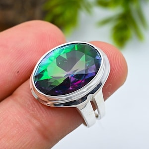 Pode incluir: Anel de prata com uma grande pedra preciosa oval com uma exibição vibrante de cores, incluindo verde, roxo e azul. A pedra é engastada numa banda de prata polida com um design de haste dividida. O anel é uma peça marcante.