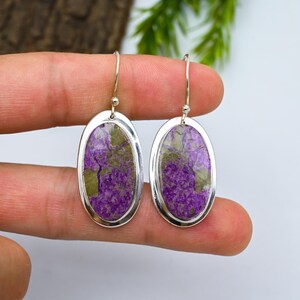 Könnte beinhalten: Ohrringe in ovaler Form mit silbernem Rahmen und einem lila-grünen Stein. Die Ohrringe haben ein einfaches Haken-Design. Der Stein hat ein einzigartiges Muster und Farbvariation.