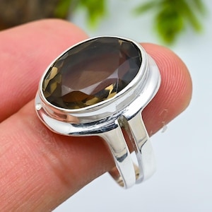 Op de afbeelding: Een zilveren ring met een grote, ovaal geslepen rookkwarts edelsteen. De edelsteen heeft een doorschijnende bruine kleur en is gezet in een gepolijste zilveren band. De ring heeft een gespleten schachtontwerp.