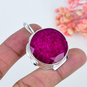 Può includere: Un ciondolo con pietra preziosa color magenta vibrante, rotondo e sfaccettato, incastonato in una montatura in argento sterling lucido. La pietra presenta una superficie cristallina e testurizzata con tonalità rosa intenso e una contromaglia.
