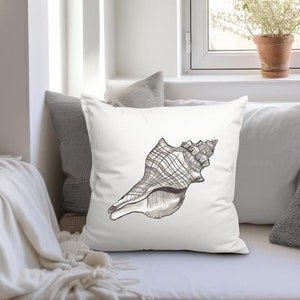 May include: Square white throw pillow featuring a detailed black and gray seashell illustration. The pillow is placed on a white couch, with other pillows and a blanket visible. A window with a plant in a terracotta pot is in the background.