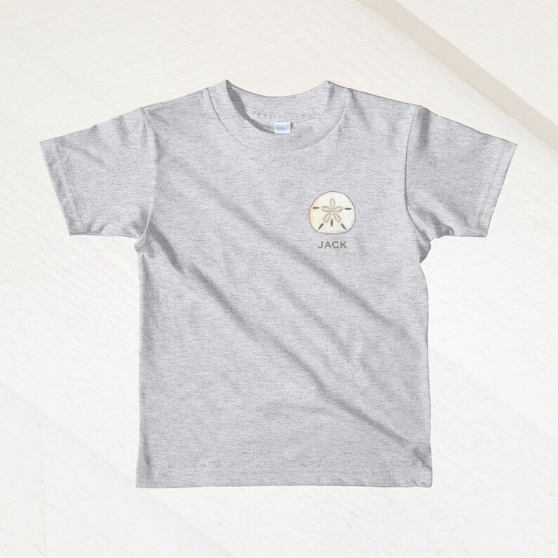 K&ouml;nnte beinhalten: Graues T-Shirt mit kurzen &Auml;rmeln, einem Sanddollar-Motiv und dem Namen "JACK" darunter.